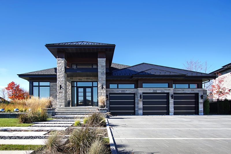 La façade d'une maison Louis-Seize à Boisbriand : pierre, toit en pente, garage triple